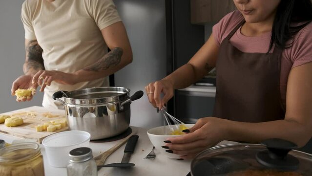 Two young latin people moulding llapingachos dough and beating eggs at kitchen.