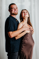 a pregnant girl in a brown dress stands in an embrace with a man