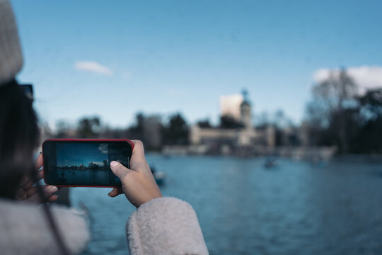 Young woman with her cell phone taking a picture of the large lake in the Retiro Park in Madrid, Spain.