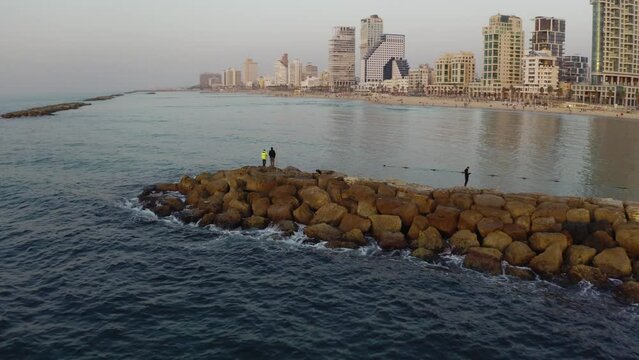 4k Aerial - Orbiting around man fishing Tel aviv beach - during sunset