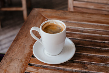 Black coffee in a large white mug on a wooden table. Hot double americano on the veranda with space for text