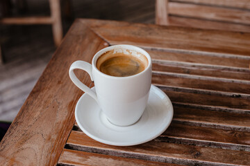 Fototapeta premium Black coffee in a large white mug on a wooden table. Hot double americano on the veranda with space for text