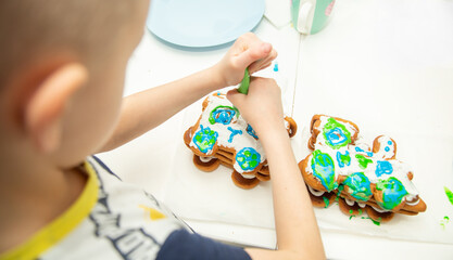 A six-year-old boy of European appearance decorates gingerbread with cream. Cooking in the kitchen