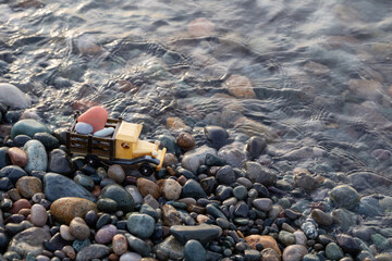 toy wooden car on the sea beach with rocks at sunset