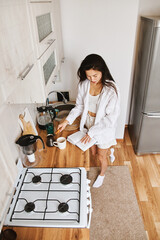 Portrait long hair brunette Asian woman in white clothes making morning hot cup coffee in kitchen - 576633412