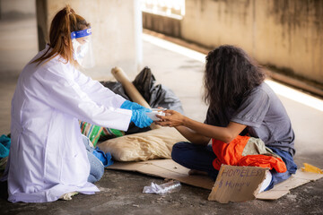 Health workers in uniforms, gloves and protective masks while helping the homeless. Depressed homeless poor help and hope concept - obrazy, fototapety, plakaty