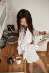 Young Asian woman drinking hot tasty beverage coffee and enjoying of reading book - 576633461