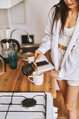 Young happy brunette woman making hot tasty beverage coffee, sweet breakfast, reading book - 576633849
