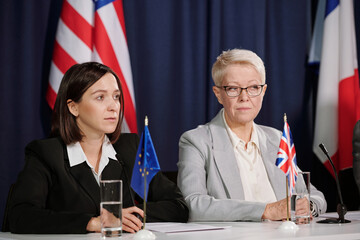 Mature and young female delegates representing European Union and Great Britain listening to...
