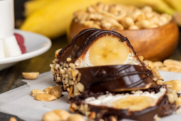 Sliced sweet cake with banana, chocolate glaze, milk filling and peanuts