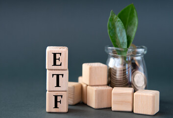 ETF - acronym on wooden cubes on the background of a glass jar with coins and green leaves