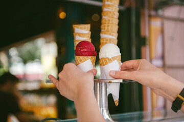 Woman shopping for ice-cream on a warm hot day waffle cone with yoghurt and cherry red ice-cream on the counter