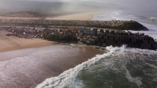 Aerial view of crashing waves against rocky wall at sandy beach with river mouth in Nazar&eacute;, Portugal - Rio Alcoa,Leira