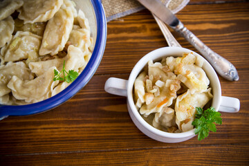 cooked dumplings with potatoes and fried onions on a wooden table.