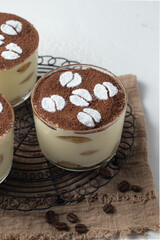 Traditional italian dessert tiramisu with savoiardi biscuits, mascarpone cheese, cream, egg yolks, amaretto liqueur and cocoa. Portion serving in glass decorated coffee beans made from powdered sugar