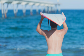 Rear view of Hispanic surfer boy standing on the beach in swimsuit looking out to sea with...