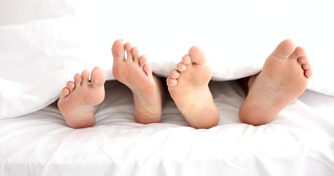 Closeup of young beautiful and loving couple playing with feet under covers