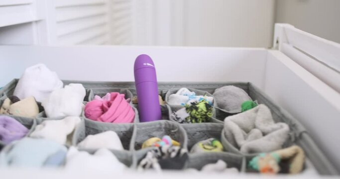 Woman's hand opens drawer with folded socks and selects a purple vibrator. Concept of obtaining sexual satisfaction at home. Storage, organizer.