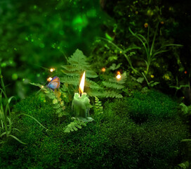 magic candle for witch ritual in forest. burning candle and butterfly close up, dark green blurred...