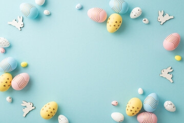 Easter decorations concept. Top view photo of colorful easter eggs and bunnies on isolated pastel blue background with copyspace in the middle