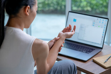 Asian woman is sitting with her laptop and her wrist aches while working at home office. Office syndrome hand pain by occupational disease. - 576650489