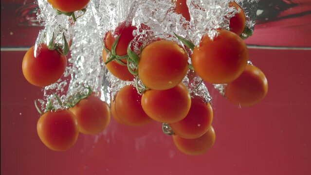 Slow motion of red cherry tomatos falling into water on red background