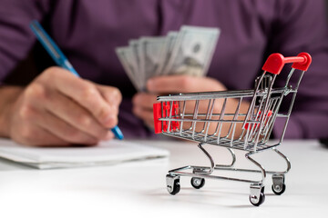 Man calculates the budget. Shopping cart a on table with calculator and paper and mohey in hadns.