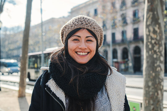 Close up portrait of young happy asian woman with beanie hat looking at camera with joyful attitude. Front view of girl standing outdoors at european city street. Lifestyle concept. High quality photo