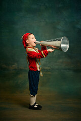Little preschool age boy dressed up as medieval little prince and pageboy shouting at megaphone...