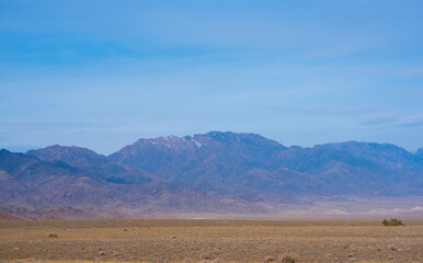 Rocky desert landscape with sparse vegetation and mountains peaks in a blue haze. Typical landscape near at Nepal Tibet border. Flat dry desert with mountains.