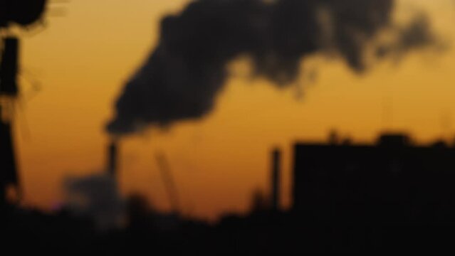 Blurred video silhouettes of CHP chimney with column of smoke and high-rise building. Orange colour of dawn. The global energy crisis. Urban landscape. Smooth departure of the camera