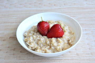 A bowl of oatmeal with strawberries on top isolated on pastel background, close-up 