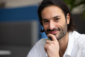 portrait d'un jeune homme de 30 ans beau et souriant. En arrière plan, il y a des plantes vertes et un bureau confortable