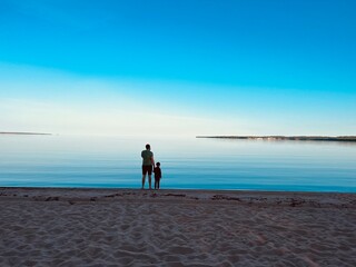 silhouette of man and child on background of sky and lake. Summer sunset