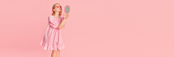 Beauty as it is. Young tender girl in pink dress looking at mirror over pink studio background. Concept of beauty, emotions, fashion, lifestyle and youth culture. Banner. Copy space for ad