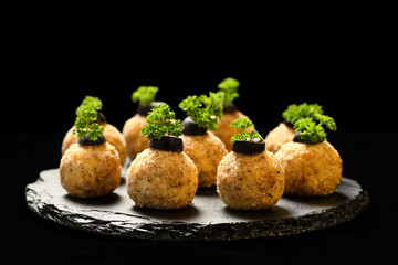 Homemade delicious ball appetizer with chicken, cheese, eggs and walnuts, decorated with parsley and olive slices, served on blackstone plateau. Black background