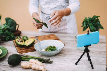 Young woman streaming online healthy food cooking lesson of green salad with vegetables and fruits - Influencer concept - Focus on right hand