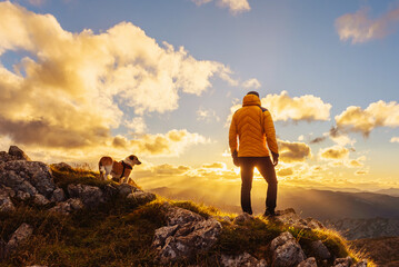 hiker with his back turned and standing on a rock contemplating a beautiful sunset on the top of a...