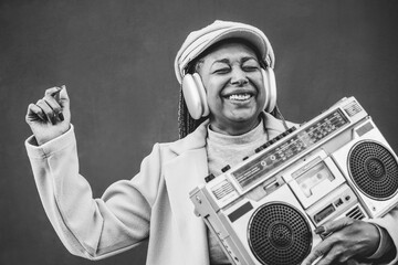 Happy african senior woman listening music in boombox vintage stereo - Focus on face - Black and...