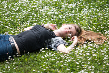 smiling young woman lying on a lawn with daisies in summer field