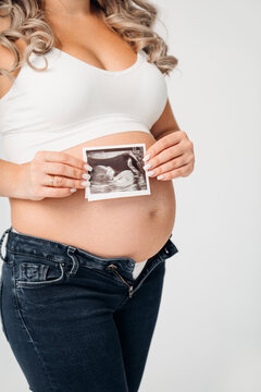a pregnant woman in a white top holding a picture of the ultrasound in his hands