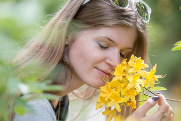 portrait of smiling girl enjoining aroma of a gentle purple flower in summer park