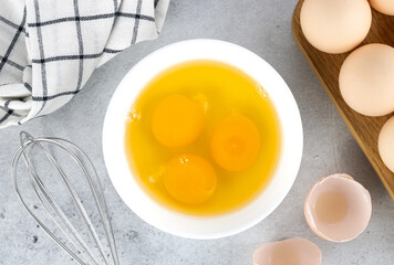 Cooking baking ingredients eggs, whisk and kitchen textiles on gray concrete background. Pie or cake recipe. Top view.