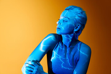 Storm. Portrait of young blonde girl with abstract neon stripes on body posing over orange...