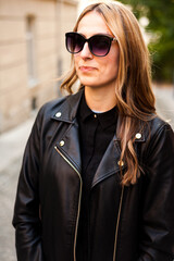 Smiling woman in the city street wearing black leather jacket and white pants and sunglasses
