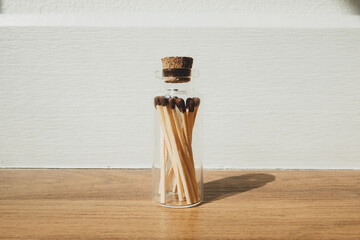 Matchstick in glass bottle on wooden floor with shadow.