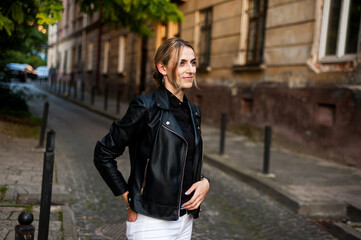 Fototapeta na wymiar Smiling woman in the city street wearing black leather jacket and white pants and sunglasses