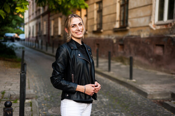 Fototapeta na wymiar Smiling woman in the city street wearing black leather jacket and white pants and sunglasses