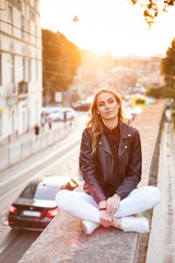 Smiling woman in the city street wearing black leather jacket and white pants and sunglasses