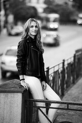 Smiling woman in the city street wearing black leather jacket and white pants and sunglasses